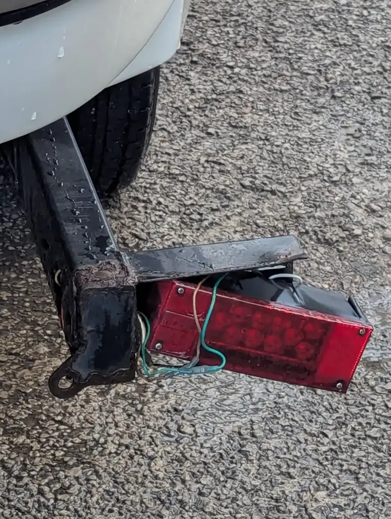 Broken LED tail light hanging from damaged wiring on the rear of a boat trailer before repair.