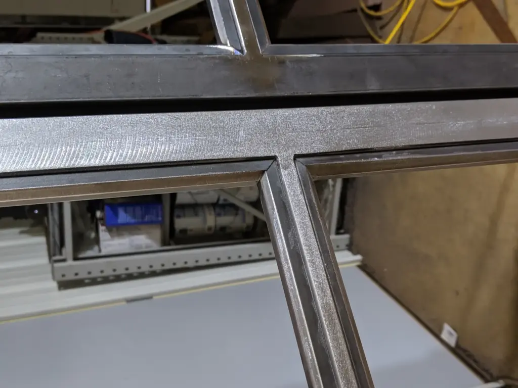 Raw welded steel frame joint on a custom Crittall-style French door before finishing
