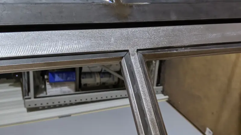 Raw welded steel frame joint on a custom Crittall-style French door before finishing