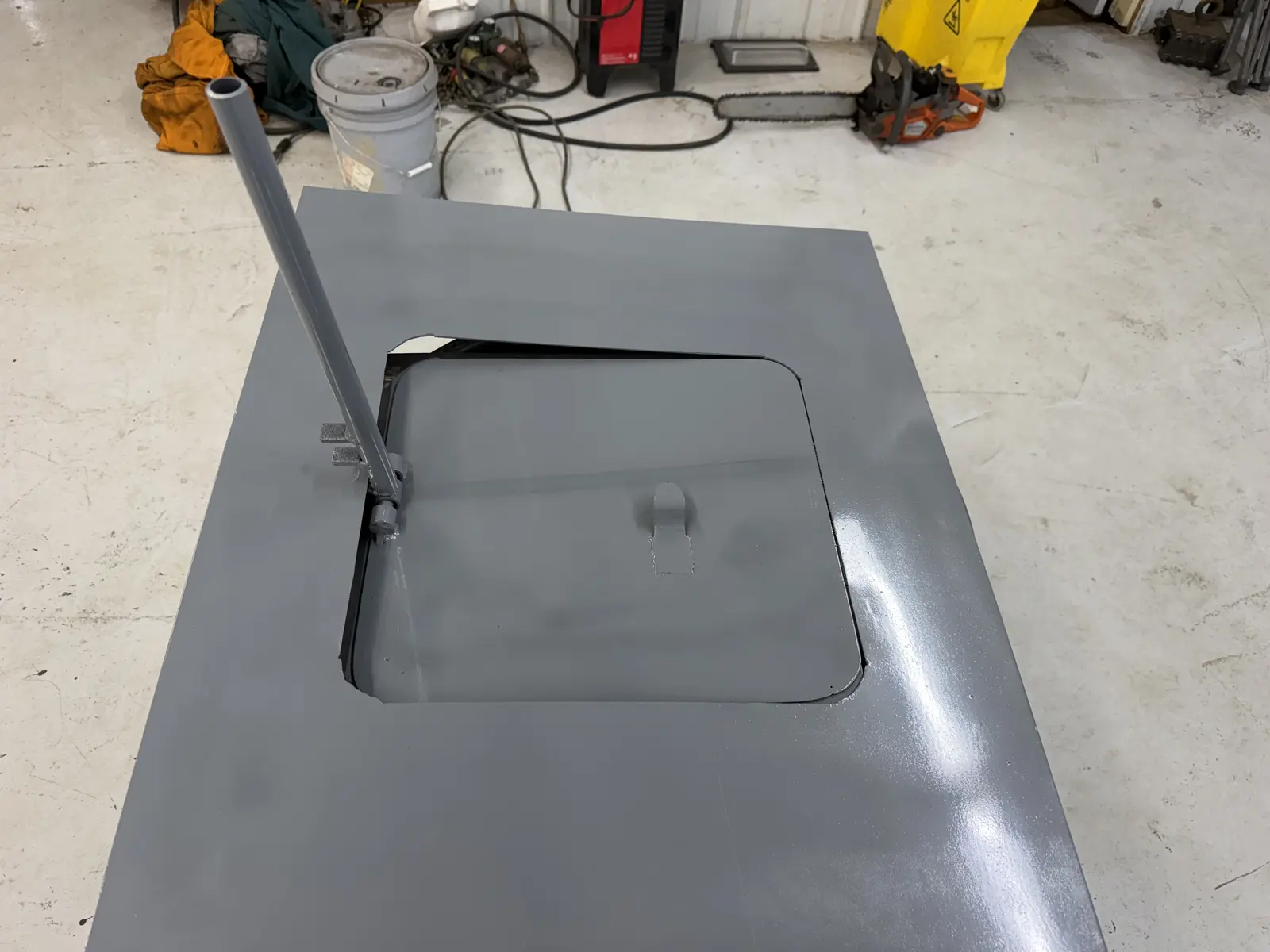 Custom air mover vent plate with the pipe lever raised and the hinged flap swung down into the opening, IronMann shop in Flint, MI