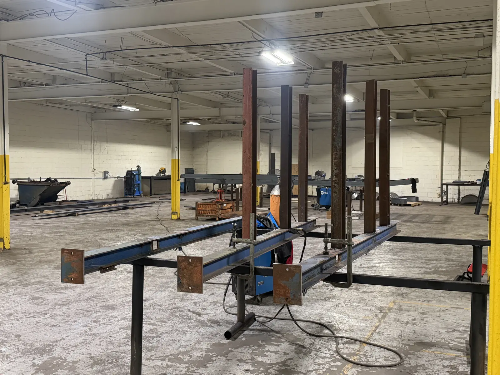 Rust-colored steel arms clamped upright on blue steel columns resting across shop stands, mid-build on a cantilever rack in Flint, MI