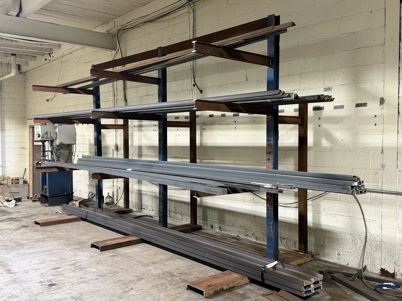 Finished cantilever steel rack against a block wall in Flint, MI, holding channel, angle and tube stock on its arms with a bundle resting on the base
