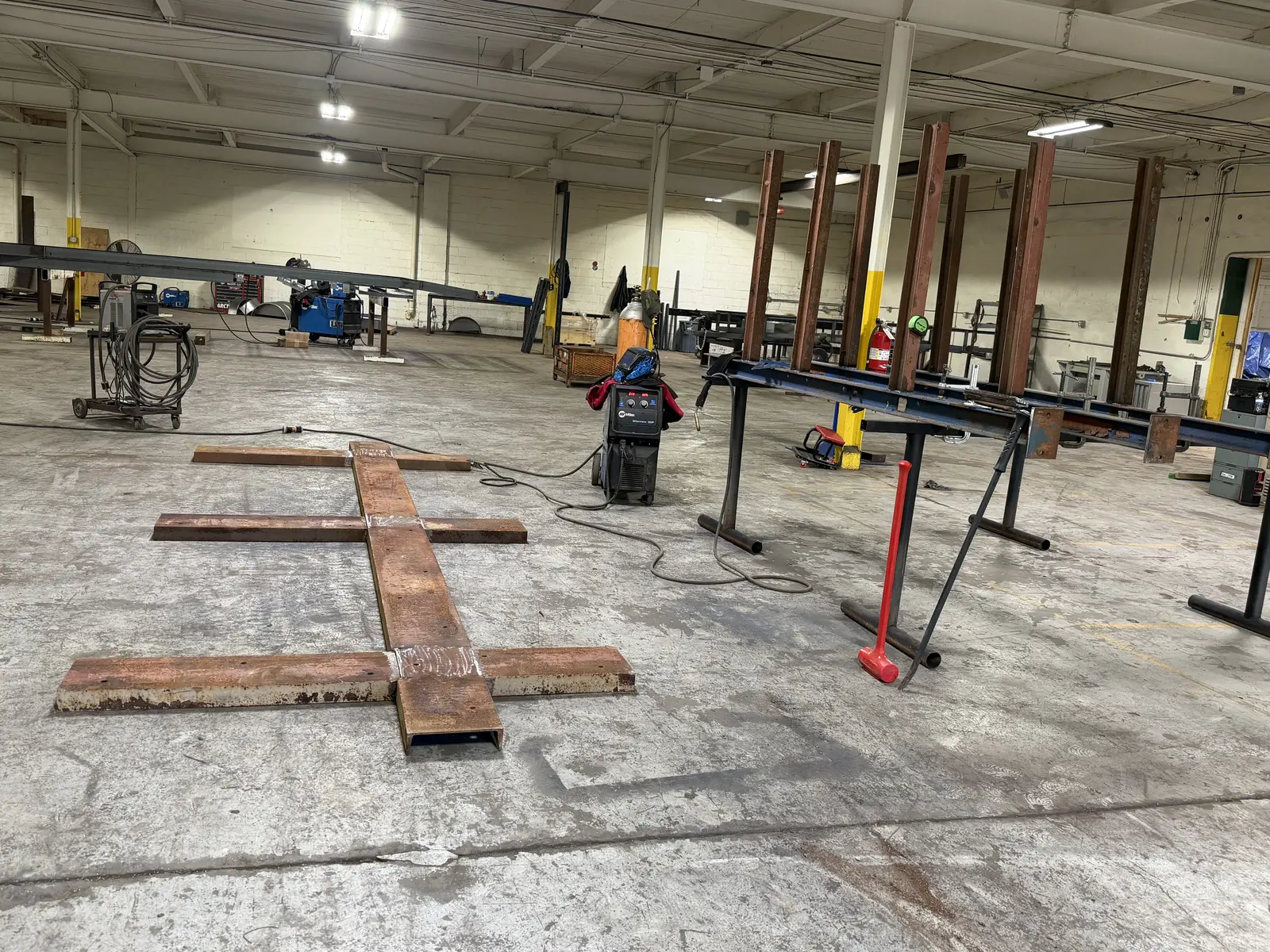 Welded C channel base for a cantilever steel rack laid out on a fab shop floor in Flint, MI, with the column assemblies on stands behind it